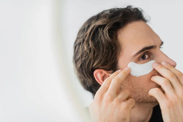 Young man applying eye patch on face at home — Stock Photo