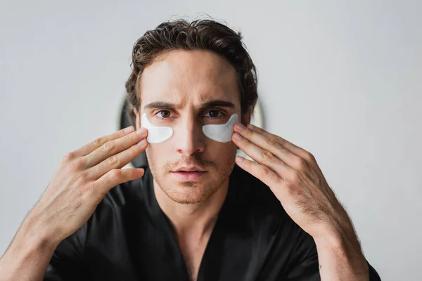 Young man in black robe applying eye patches at home — Stock Photo
