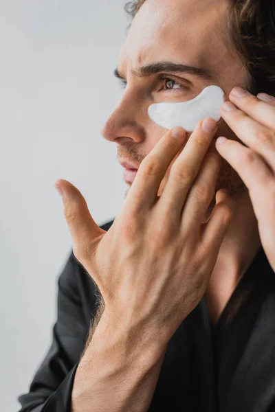 Man in silk robe applying eye patch isolated on grey — Stock Photo