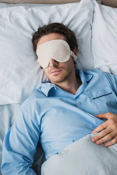 Vista superior do homem no pijama e máscara de sono dormindo na cama em casa — Fotografia de Stock