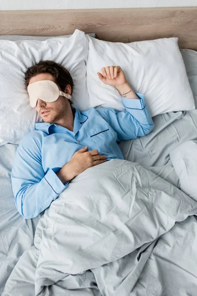 Vista dall'alto dell'uomo in maschera e pigiama che dorme sul letto — Foto stock