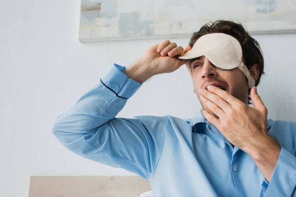 Hombre con máscara para dormir y pijama bostezando en casa - foto de stock