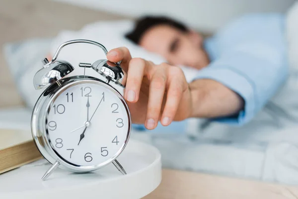 Blurred man switching alarm clock on bedside table in morning — Stock Photo