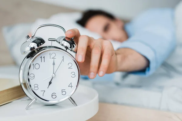 Hombre borroso cambiando el despertador en la mesita de noche por la mañana - foto de stock