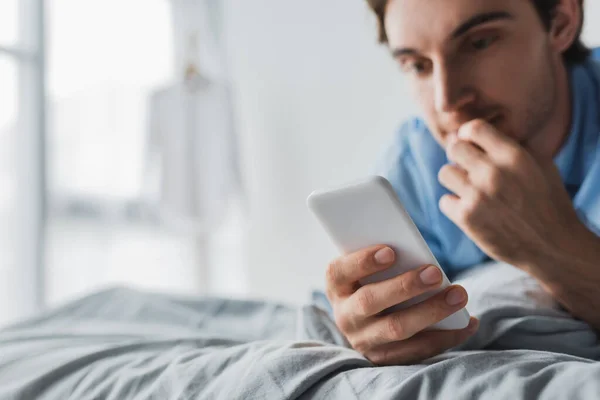 Smartphone in mano di uomo sfocato sul letto al mattino — Foto stock