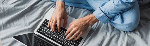 Cropped view of man in pajama using laptop on bed, banner — Stock Photo