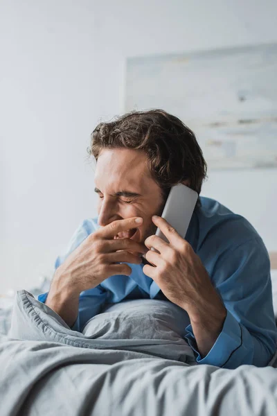 Fröhlicher Mann im Pyjama plaudert morgens auf dem Bett mit Smartphone — Stockfoto