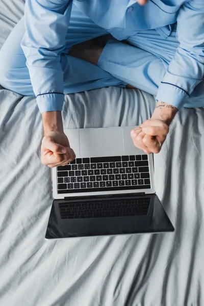 Vista superior del freelancer en pijama mostrando sí gesto cerca de la computadora portátil en la cama - foto de stock