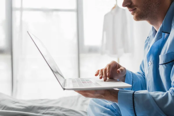 Vista ritagliata del giovane in pigiama utilizzando il computer portatile sul letto al mattino — Foto stock