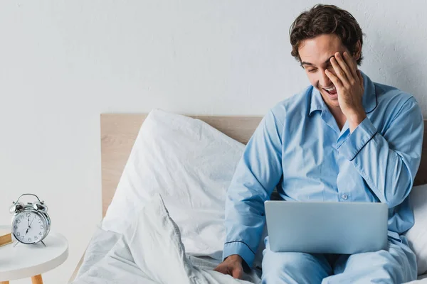 Fröhlicher Mann im Pyjama blickt morgens auf Laptop im Bett — Stockfoto