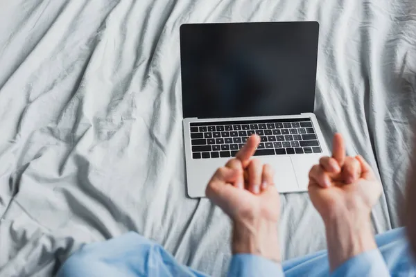 Vista recortada del freelancer en pijama mostrando los dedos medios en el portátil en la cama - foto de stock