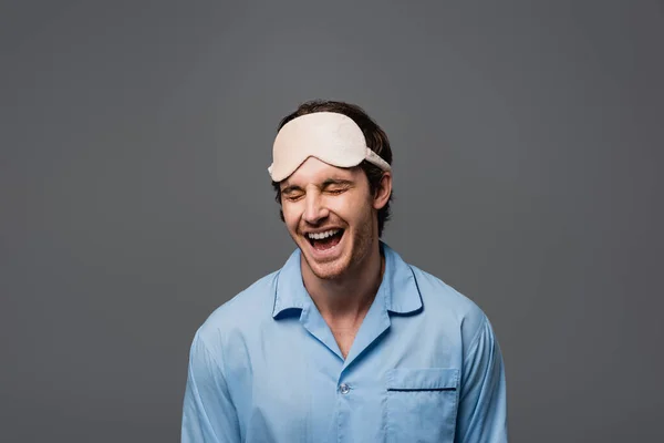 Homme heureux en masque de sommeil et pyjama isolé sur gris — Photo de stock