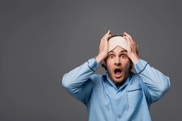 Surprised man in pajama and sleep mask looking at camera isolated on grey — Stock Photo