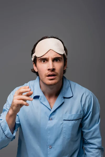 Uomo confuso in maschera del sonno e pigiama guardando la fotocamera isolata su grigio — Foto stock