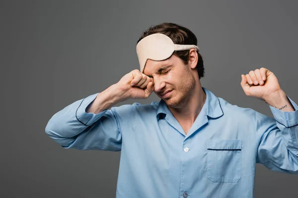 Giovane in pigiama e maschera del sonno che si estende isolato su grigio — Foto stock