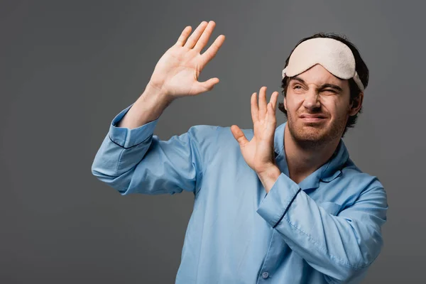 Hombre disgustado en pijama y máscara de dormir mirando hacia otro lado aislado en gris - foto de stock