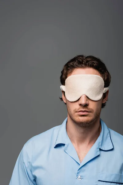 Young man in pajama and sleep mask standing isolated on grey — Stock Photo