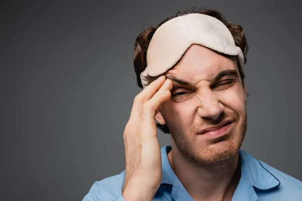 Dissatisfied man in pajama and sleep mask looking at camera isolated on grey — Stock Photo