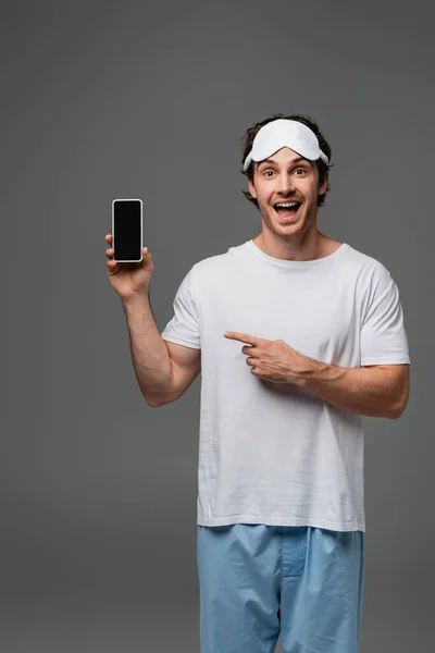 Fröhlicher Mann im Pyjama zeigt auf Smartphone mit leerem Bildschirm — Stockfoto