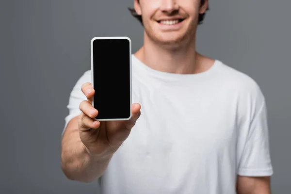 Vista recortada del teléfono inteligente en la mano del hombre sonriente borroso aislado en gris - foto de stock