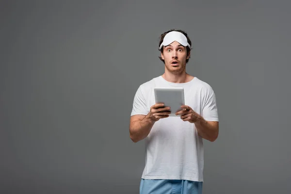 Shocked man in sleep mask and pajama using digital tablet isolated on grey — Stock Photo