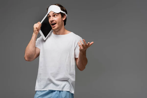 Jeune homme en masque de sommeil et pyjama parlant sur tablette numérique isolé sur gris — Photo de stock