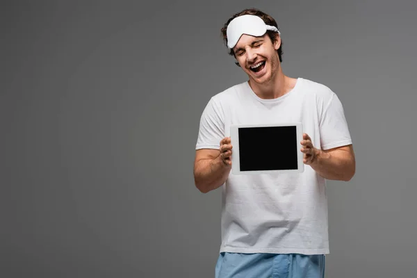 Aufgeregter Mann mit Schlafmaske hält digitales Tablet mit leerem Bildschirm isoliert auf grau — Stockfoto