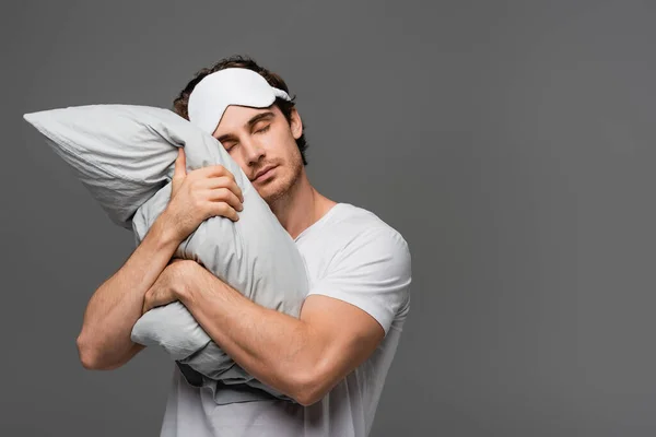 Young man in sleep mask hugging pillow isolated on grey — Stock Photo