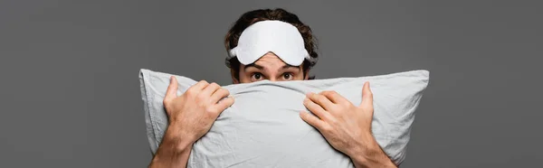 Человек в маске сна покрывает лицо подушкой, изолированной на сером, баннер — стоковое фото