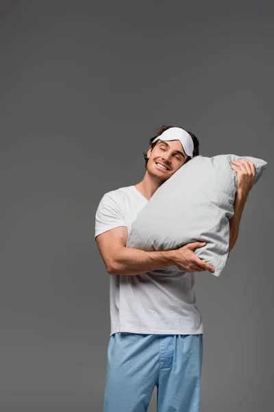 Felice uomo in pigiama tenendo cuscino isolato su grigio — Foto stock