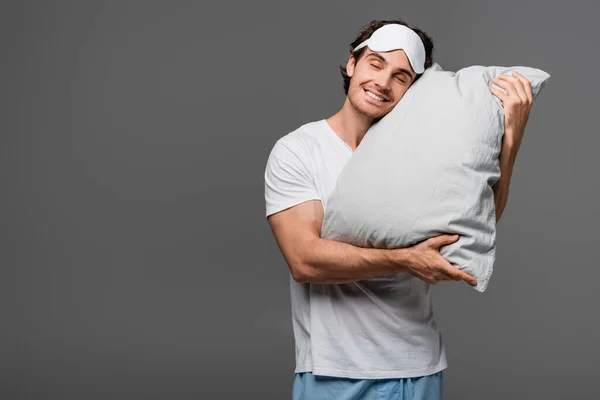 Giovane in maschera del sonno abbracciando cuscino isolato su grigio — Foto stock