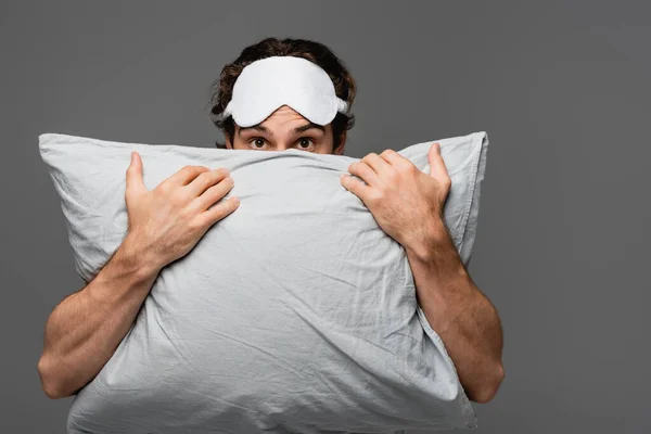 Jeune homme en masque de sommeil couvrant le visage avec oreiller isolé sur gris — Photo de stock