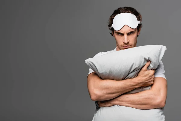 Uomo sconvolto in maschera del sonno abbracciando cuscino isolato su grigio — Foto stock