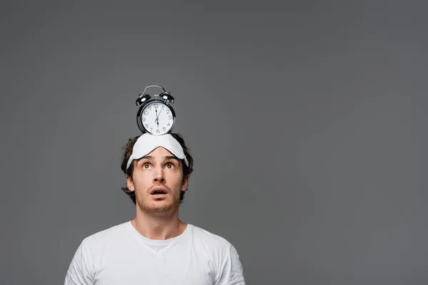 Schockierter Mann mit Schlafmaske blickt auf Wecker am Kopf isoliert auf grau — Stockfoto