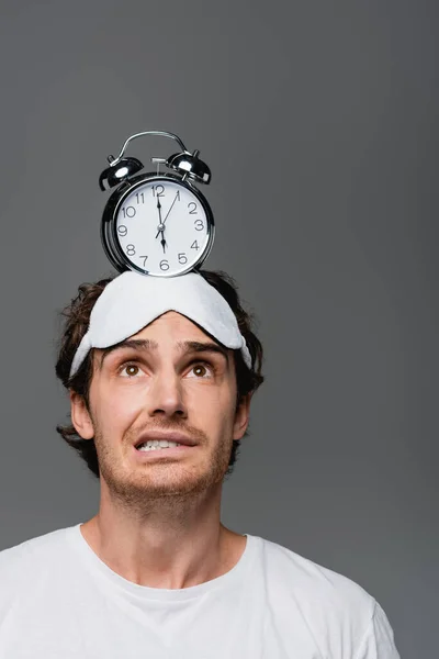 Uomo preoccupato in maschera di sonno guardando sveglia sulla testa isolato su grigio — Foto stock