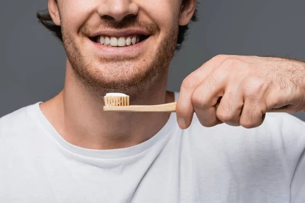 Cropped view of smiling man holding toothbrush with toothpaste isolated on grey — Stock Photo