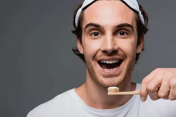 Positive man in sleep mask and white t-shirt holding toothbrush isolated on grey — Stock Photo