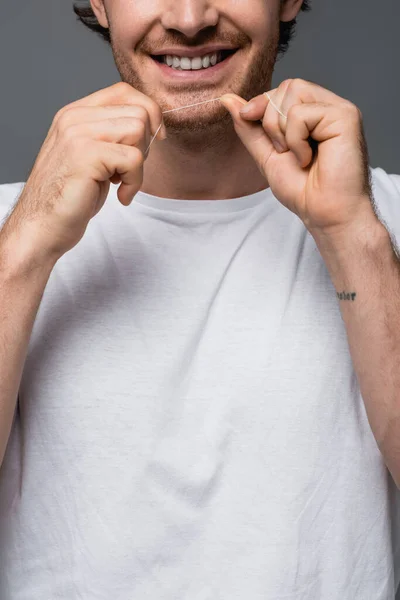 Ausgeschnittene Ansicht eines positiven Mannes im weißen T-Shirt, der Zahnseide isoliert auf grau hält — Stockfoto