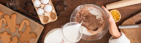 Vista ritagliata della donna afro-americana che versa latte nella farina con cacao vicino ai biscotti di Natale, banner — Foto stock