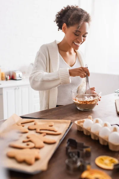 Heureuse femme afro-américaine cuisinant près des œufs brouillés et des biscuits de Noël savoureux dans la cuisine — Photo de stock