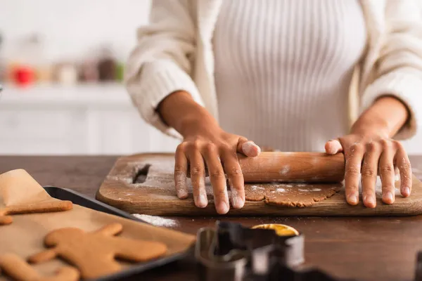 Ausgeschnittene Ansicht einer afrikanisch-amerikanischen Frau, die Teig in der Nähe von verschwommenen Weihnachtsplätzchen rollt — Stockfoto