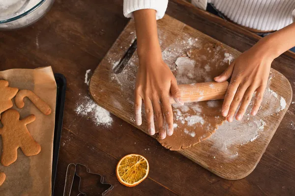 Vue recadrée de la femme afro-américaine rouler la pâte près de tranches d'orange sèches et biscuits de Noël dans la cuisine — Photo de stock