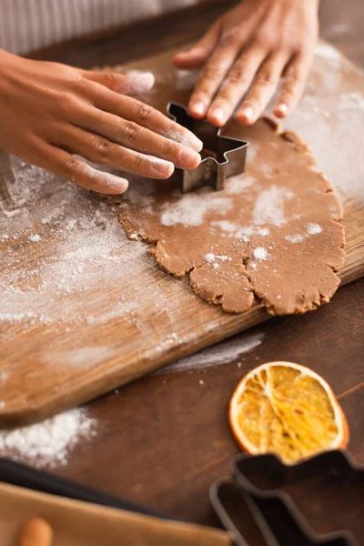 Vista recortada de la mujer afroamericana presionando cortador de galletas de Navidad en la masa en la cocina - foto de stock