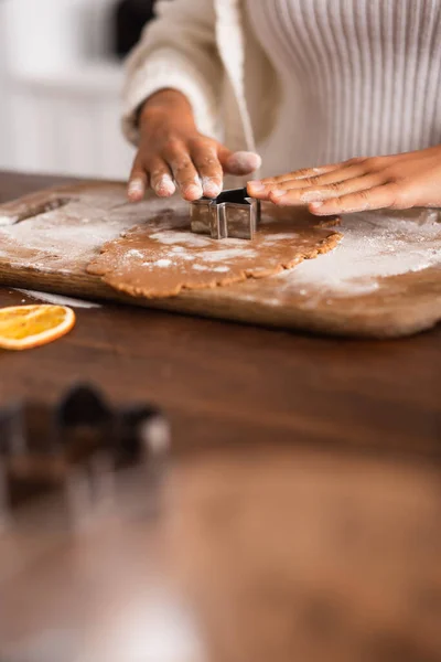 Vista ritagliata della donna afro-americana che tiene la taglierina del biscotto sulla pasta vicino alla fetta di arancia secca in cucina — Foto stock