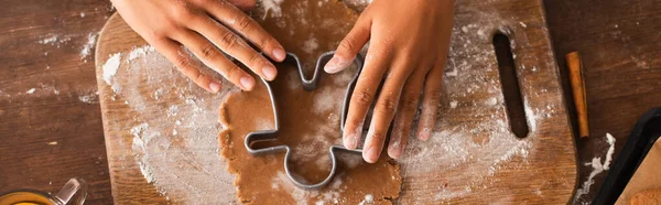 Top view of african american woman holding christmas cookie cutter on dough on cutting board, banner — Stock Photo