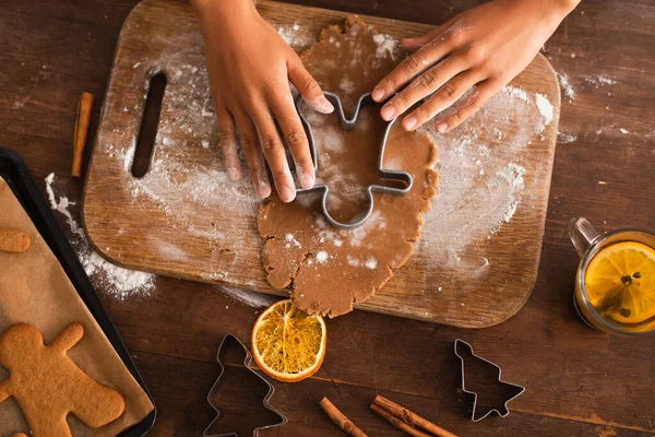 Vista superior de la mujer afroamericana presionando cortador de galletas de Navidad en la masa cerca de palitos de canela en la cocina - foto de stock