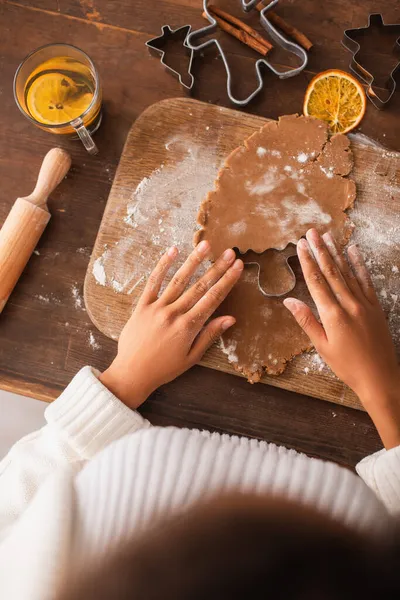 Top view of african american woman holding christmas cookie cutter on dough near tea and cinnamon sticks — Stock Photo