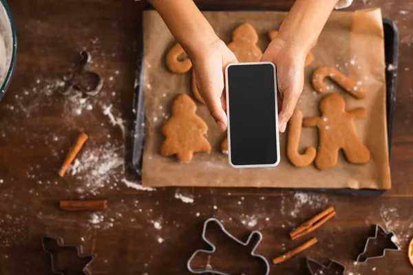 Top view of african american woman taking photo on smartphone near blurred christmas cookies — Stock Photo