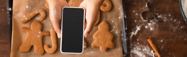 Top view of african american woman taking photo of christmas cookies on smartphone in kitchen, banner — Stock Photo