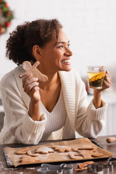 African american woman holding homemade christmas gingerbread and tea in kitchen — Stock Photo